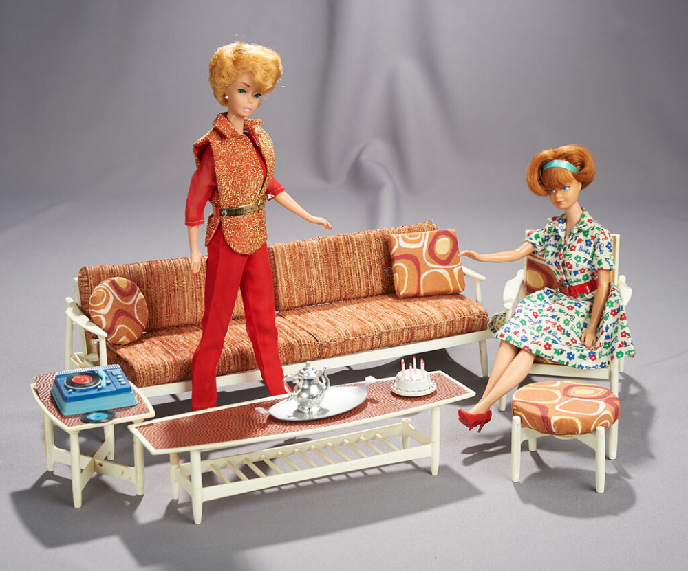 A Barbie doll stands in front of a mod-style couch while another sits on a chair